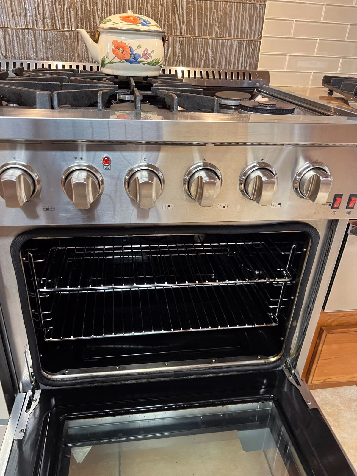 A stainless steel stove and oven interior showing the completed deep oven cleaning with sparkling racks and a clear glass door.
